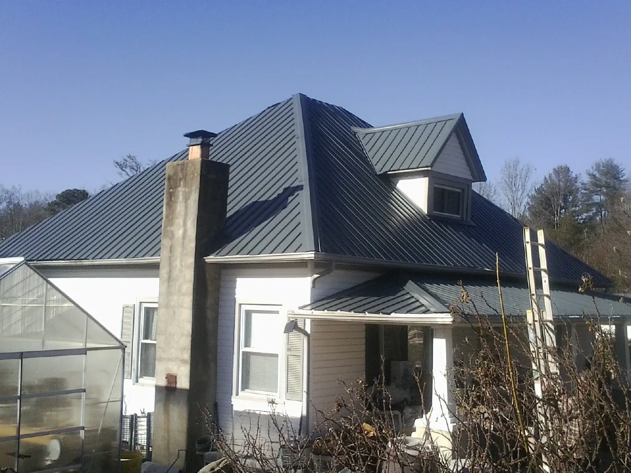 Dark blue standing seam metal roof on a white farmhouse with dormer — Slate & Tile Roof Repair by Roofing Brothers in Genesee Depot