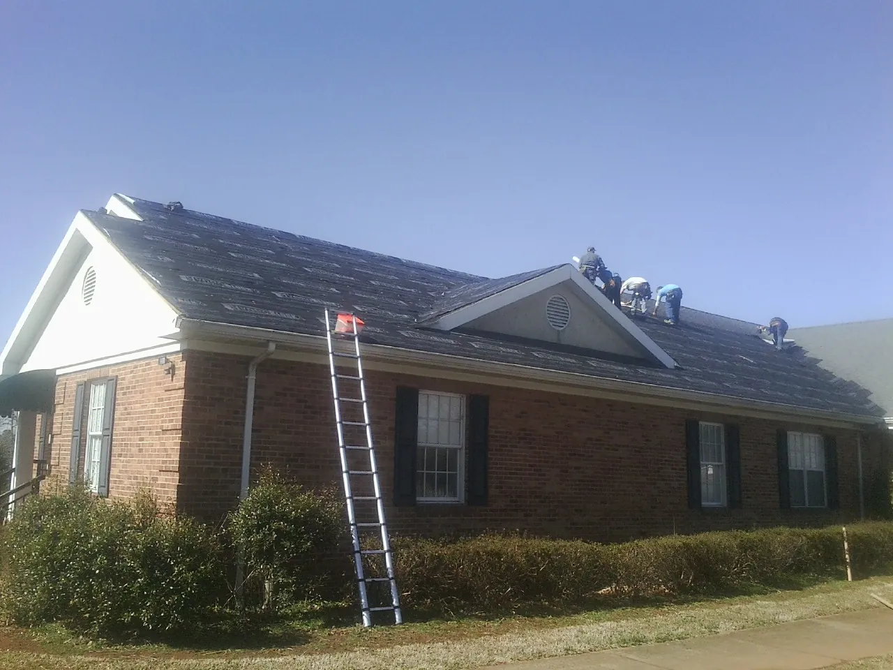 Crew tearing shingles off a brick ranch roof with a ladder set — Emergency Roof Repair work by our crew in Genesee Depot