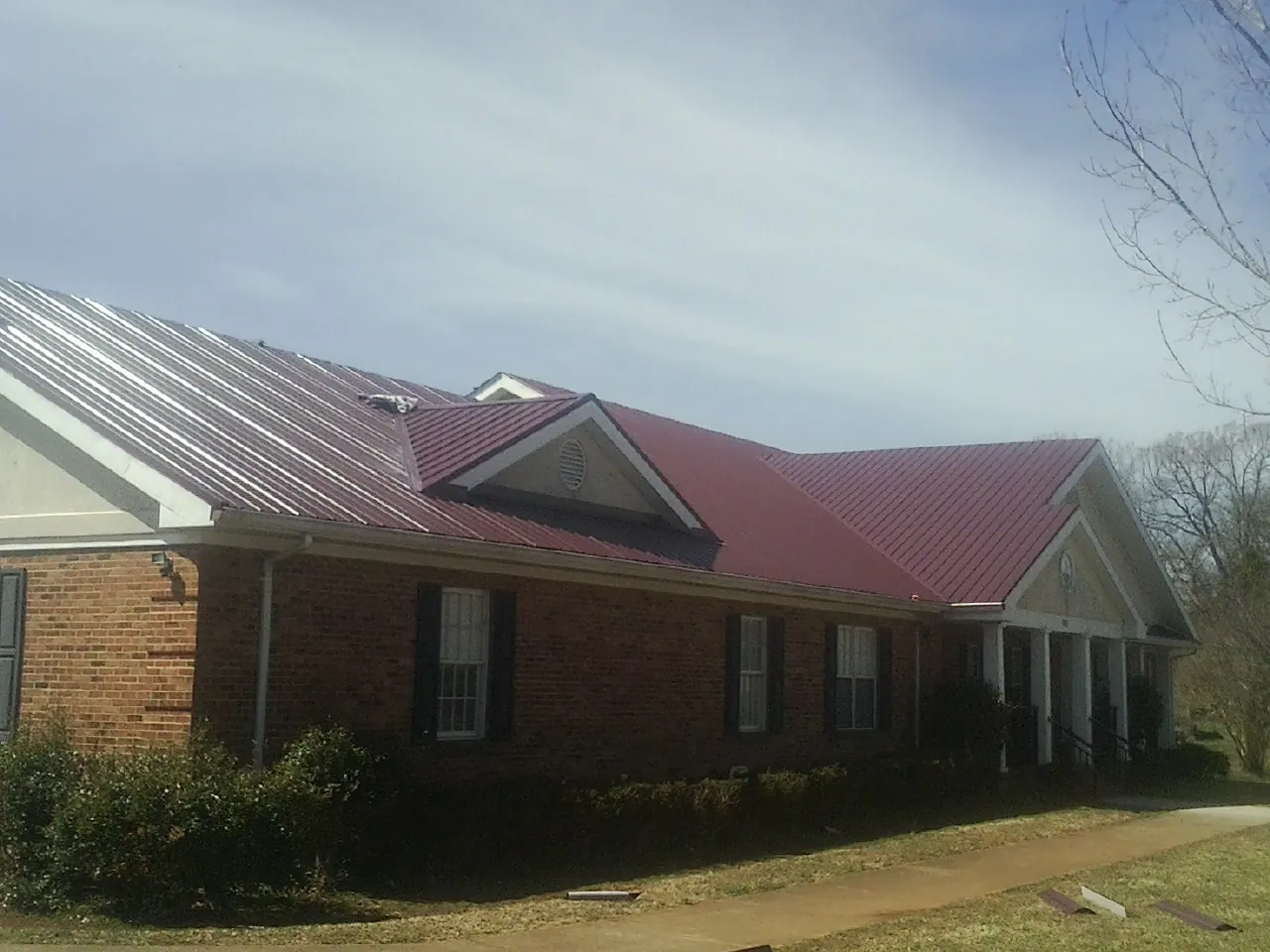 Red metal roof with gabled entries on a long brick building, from a Hail Damage Roof Repair job in Genesee Depot