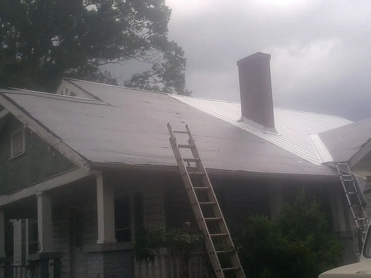 Ladders against a metal roof on an older home with a brick chimney in Genesee Depot