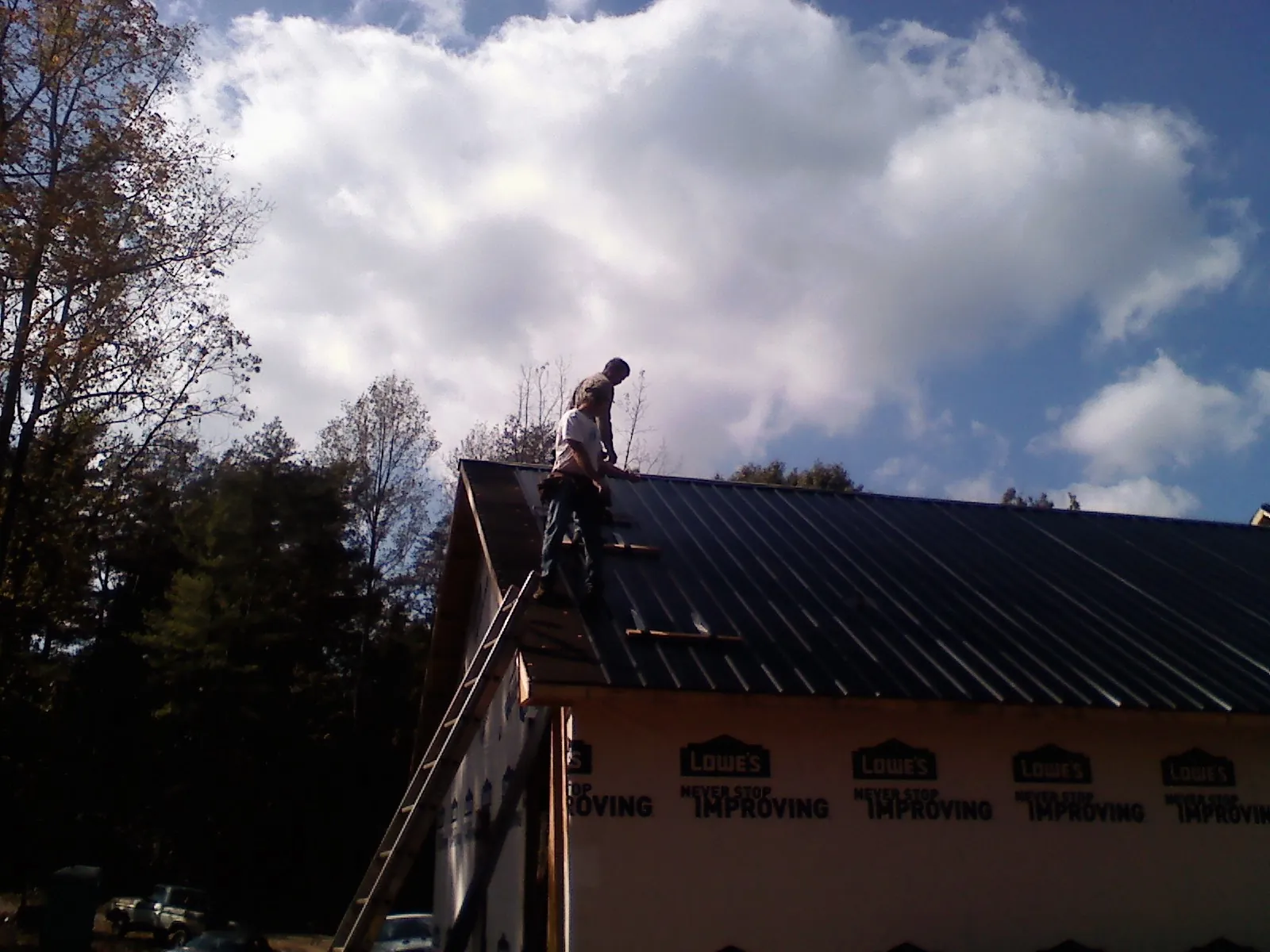Roofer fastening dark metal panels high against a cloudy sky, from a Roof Inspection job in Genesee Depot