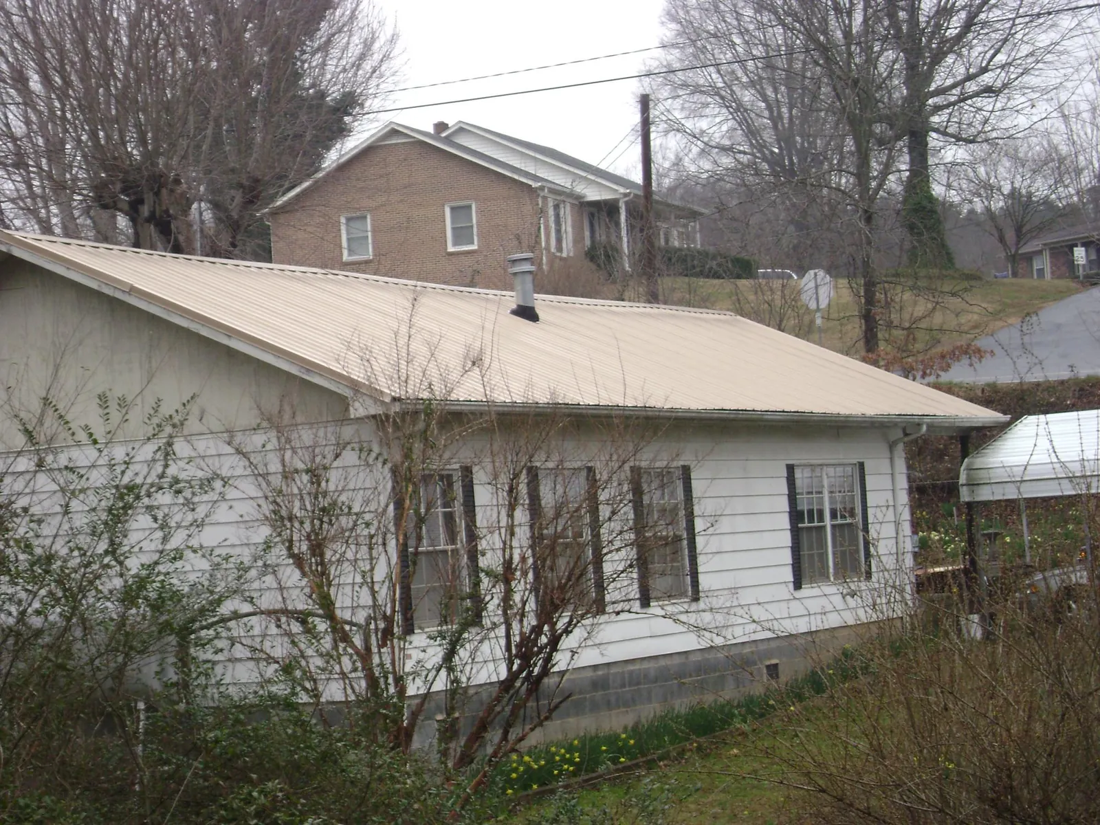 Tan metal roof on a white sided house set into a hillside — Commercial Roofing by Roofing Brothers in Genesee Depot